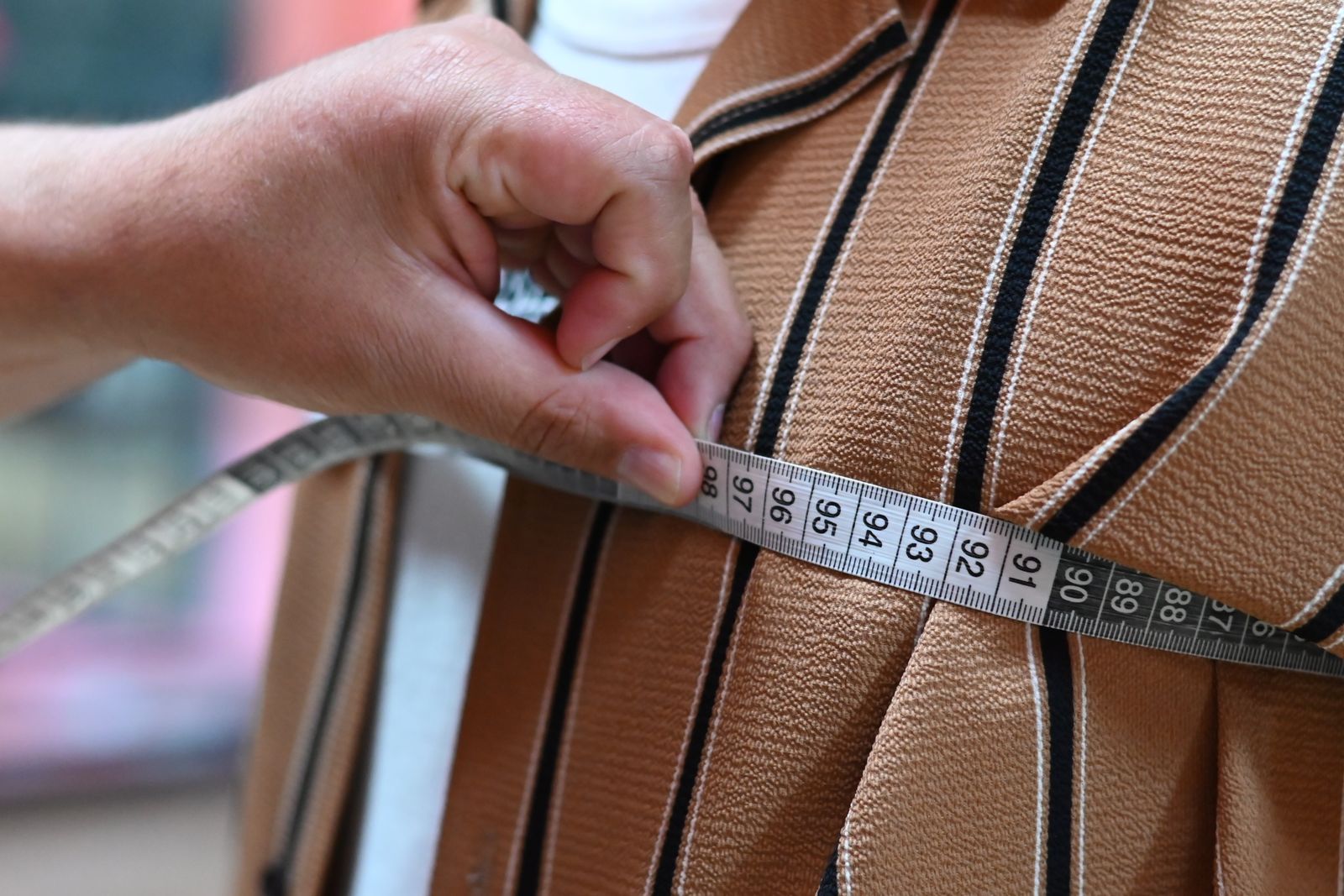 Hand holding a measuring tape against woven fabric