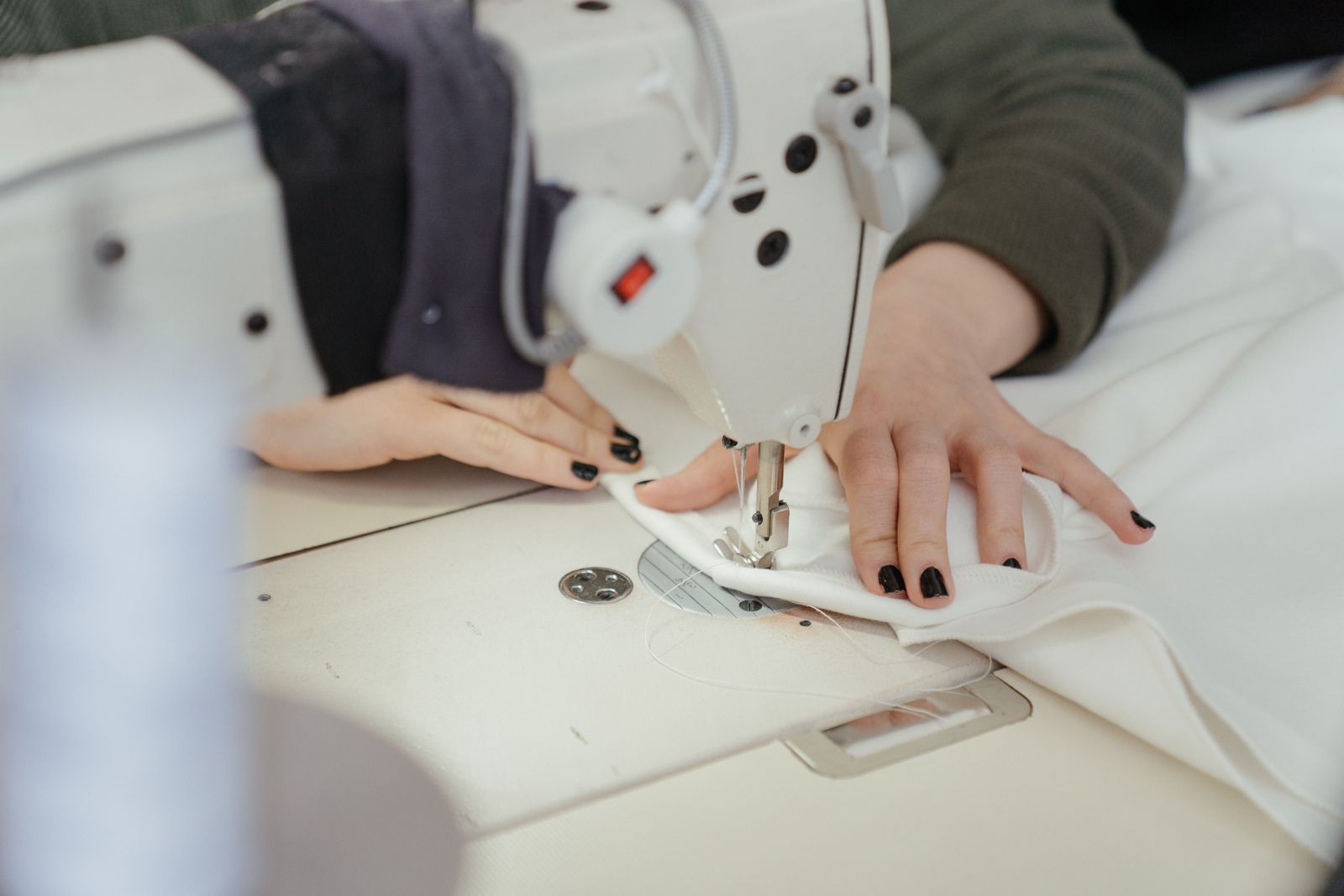 Hands guiding white fabric through an industrial sewing machine