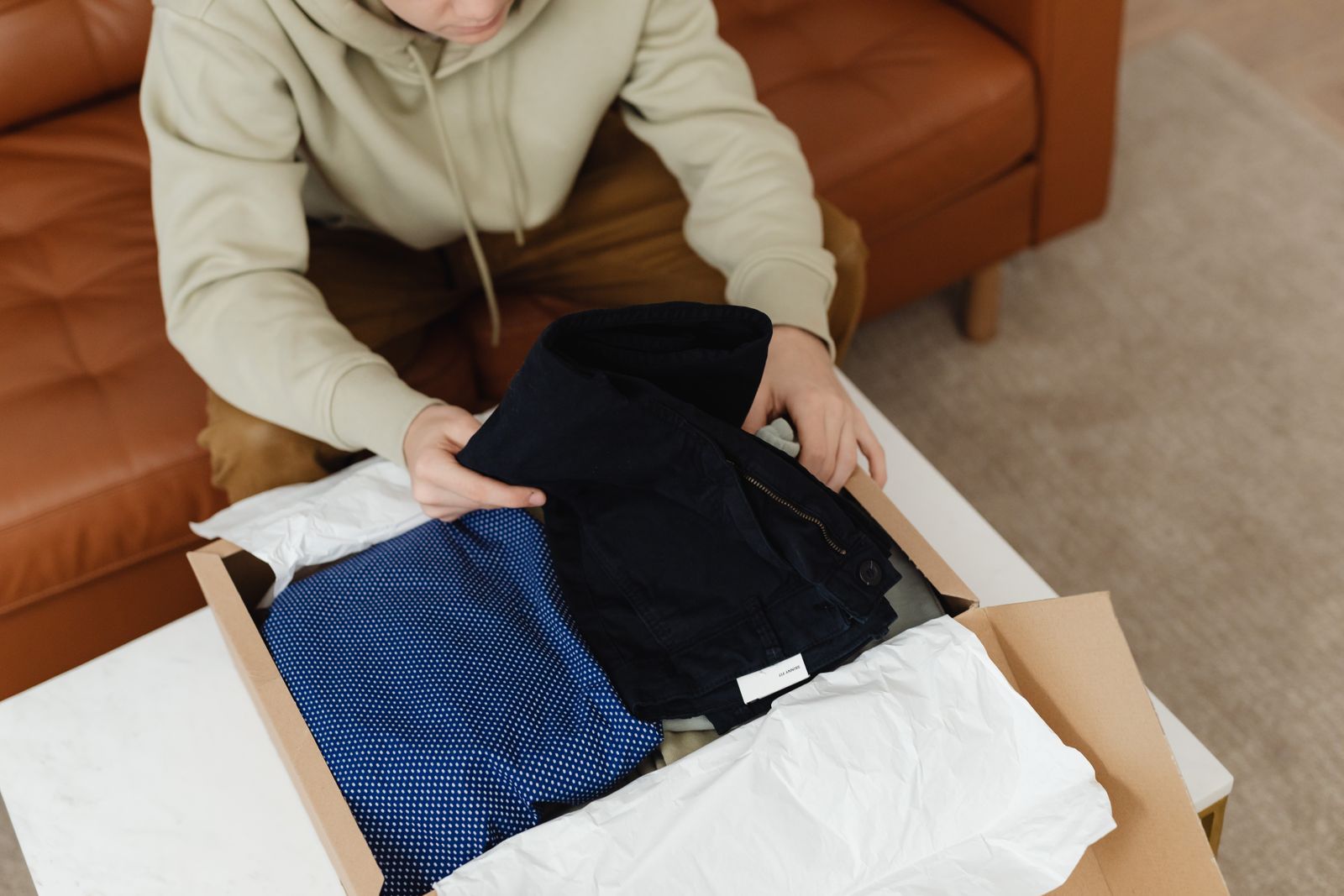 Person packing folded clothes into a cardboard box with tissue paper
