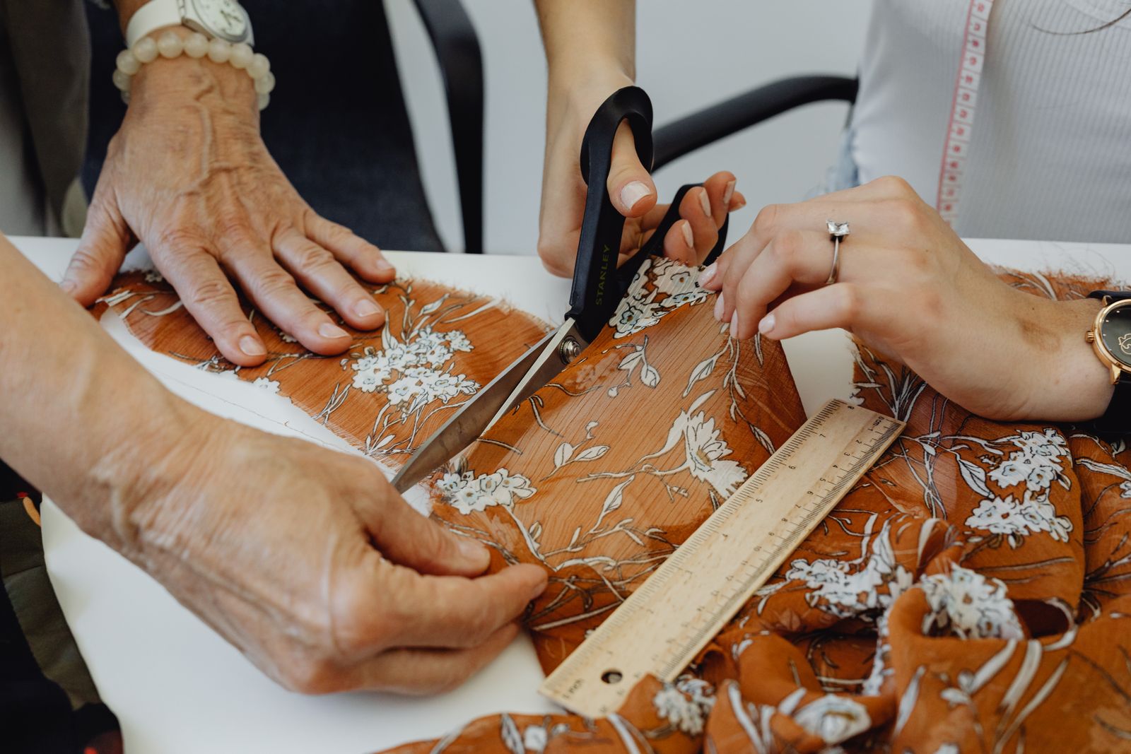 Two people cutting floral fabric with scissors and a ruler