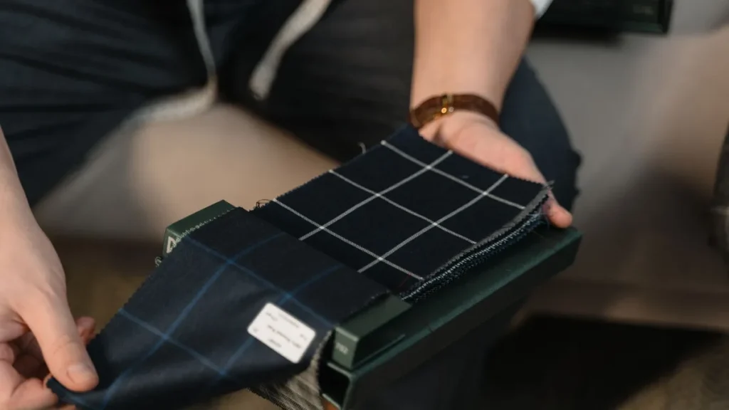 Hands comparing checked suiting fabric swatches for a tailored garment